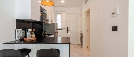 Una cocina moderna con una isla central, dos taburetes de bar y una lámpara colgante.