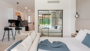 Une chambre d’hôtel moderne dotée d’un grand lit, d’un coin salon avec deux fauteuils, d’un bureau et offrant une vue sur la piscine grâce à une paroi en verre.