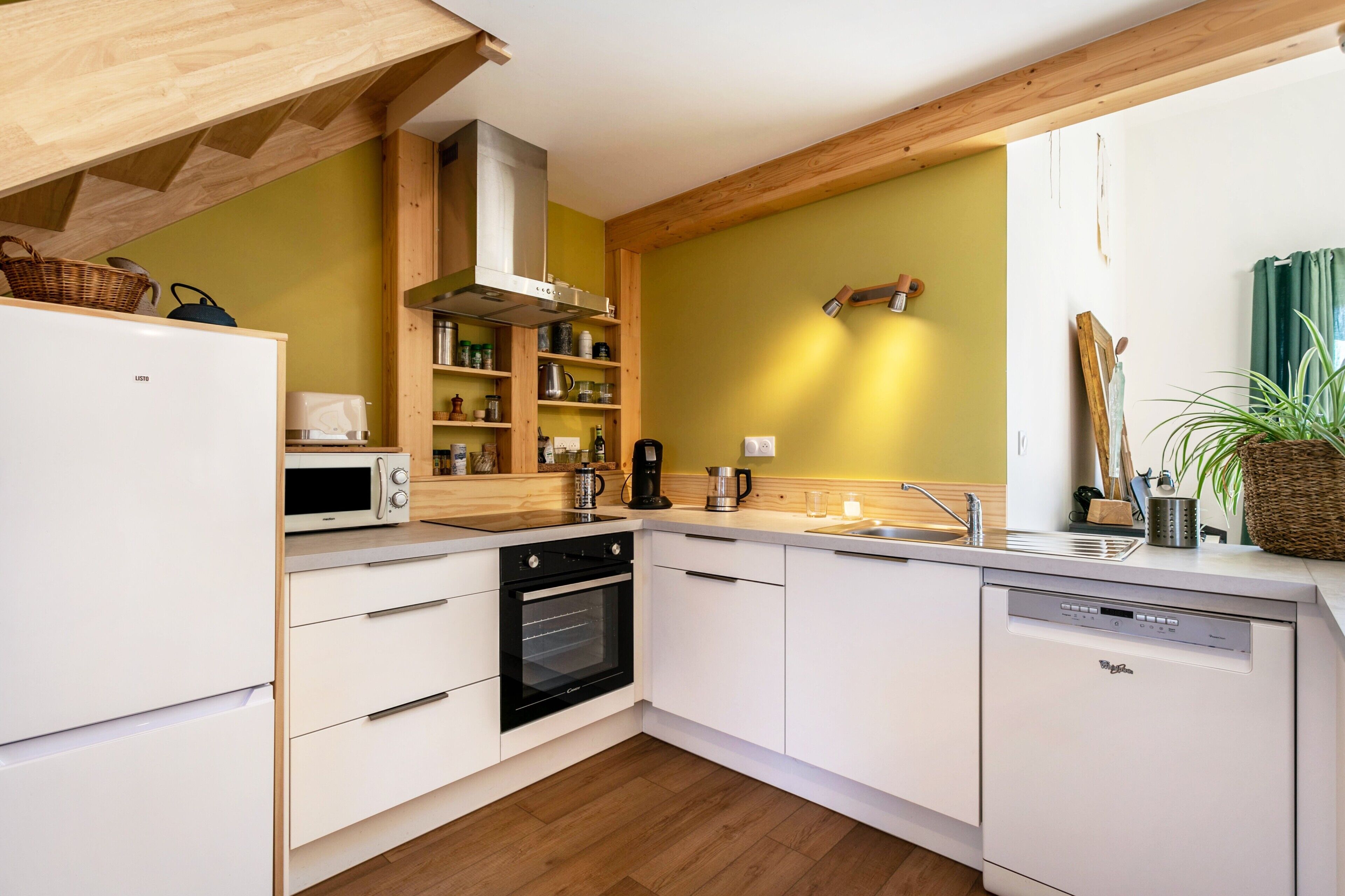A modern kitchen with white cabinetry, a built-in oven, microwave, and dishwasher, wooden beams, and a yellow wall.