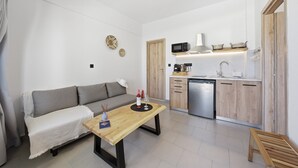 Ein kompakter Wohnraum mit Sofa, Holztisch, Küchenzeile mit Mikrowelle und Geschirrspüler.