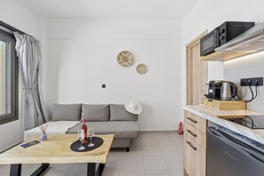A compact living space with a kitchenette, a dining area with a table, a sofa, and a wall clock. - Holiday Home 'One Bedroom Apartment with Veranda' with Balcony, Wi-Fi and Air Conditioning (Melitiei)