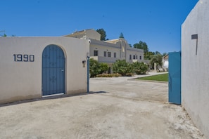 A building with a blue gate marked '1990' and a paved driveway leading to it. - Holiday Home 'One Bedroom Apartment with Veranda' with Balcony, Wi-Fi and Air Conditioning (Melitiei)