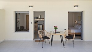Ein modernes Interieur mit Essbereich, zwei Korbstühle, einem kleinen Tisch mit einer Vase und einer durchgehenden Tür erkennbaren Küche.