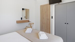Una habitación de hotel moderna con una cama, un armario de madera, un televisor montado en la pared y un espejo sobre la cama.