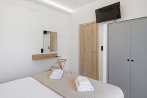 Une chambre d’hôtel moderne, équipée d’un lit, d’une armoire en bois, d’un téléviseur fixé au mur et d’un miroir au-dessus du lit.
