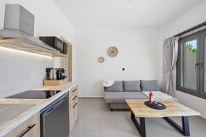 Une cuisine compacte équipée d’un four à micro-ondes, d’une cuisinière et d’un lave-vaisselle, une table à manger avec une bouteille et des verres, un canapé et une grande fenêtre.