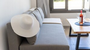 Una sala de estar moderna con un sofá gris, un sombrero blanco sobre el reposabrazos y una mesa con una botella y vasos.