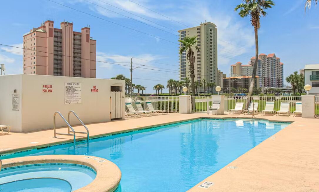 A swimming pool with a no glass pool area sign, lounge chairs, and palm trees.