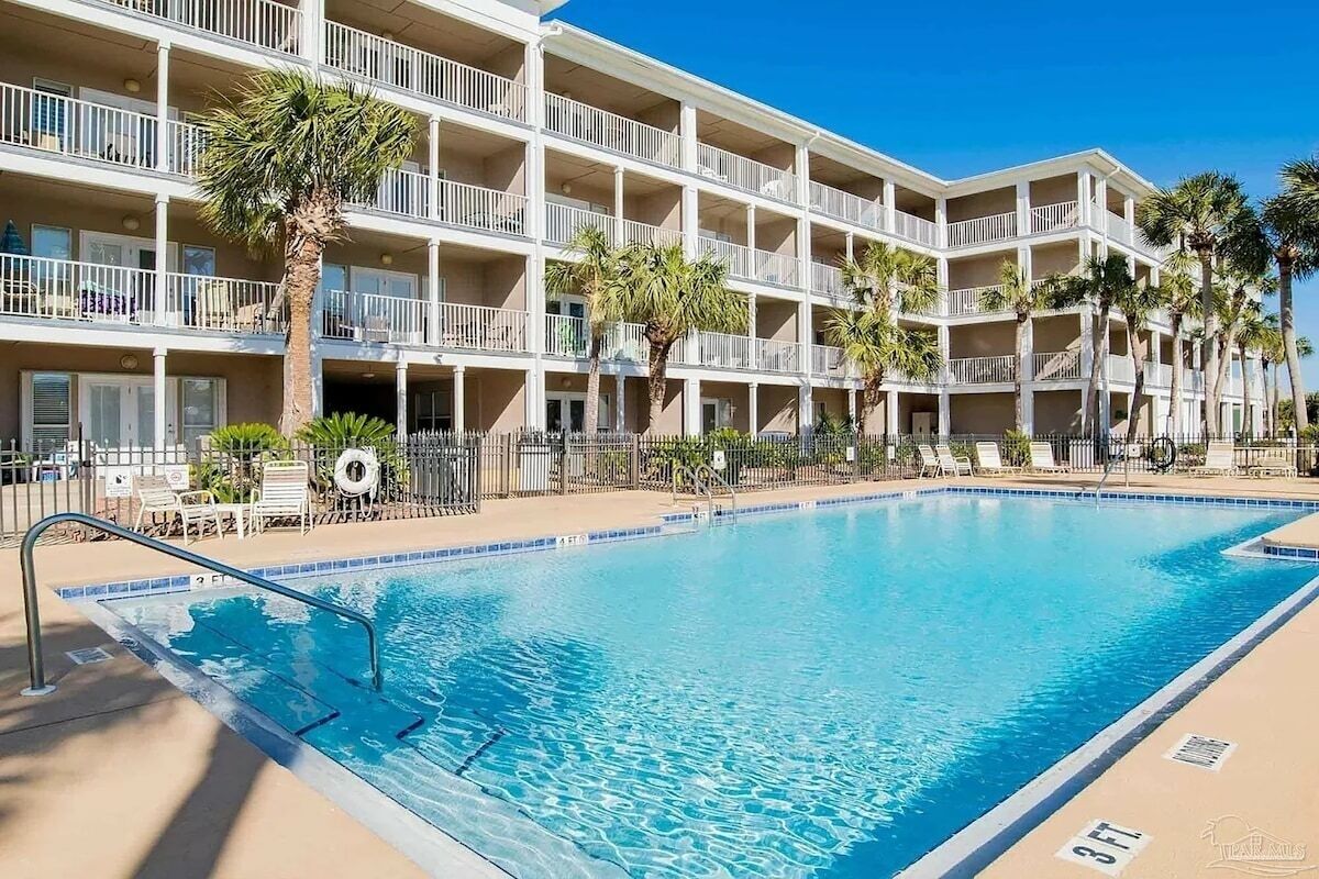 Un hôtel à plusieurs étages doté d’une piscine, de palmiers et surplombant un ciel bleu azur.