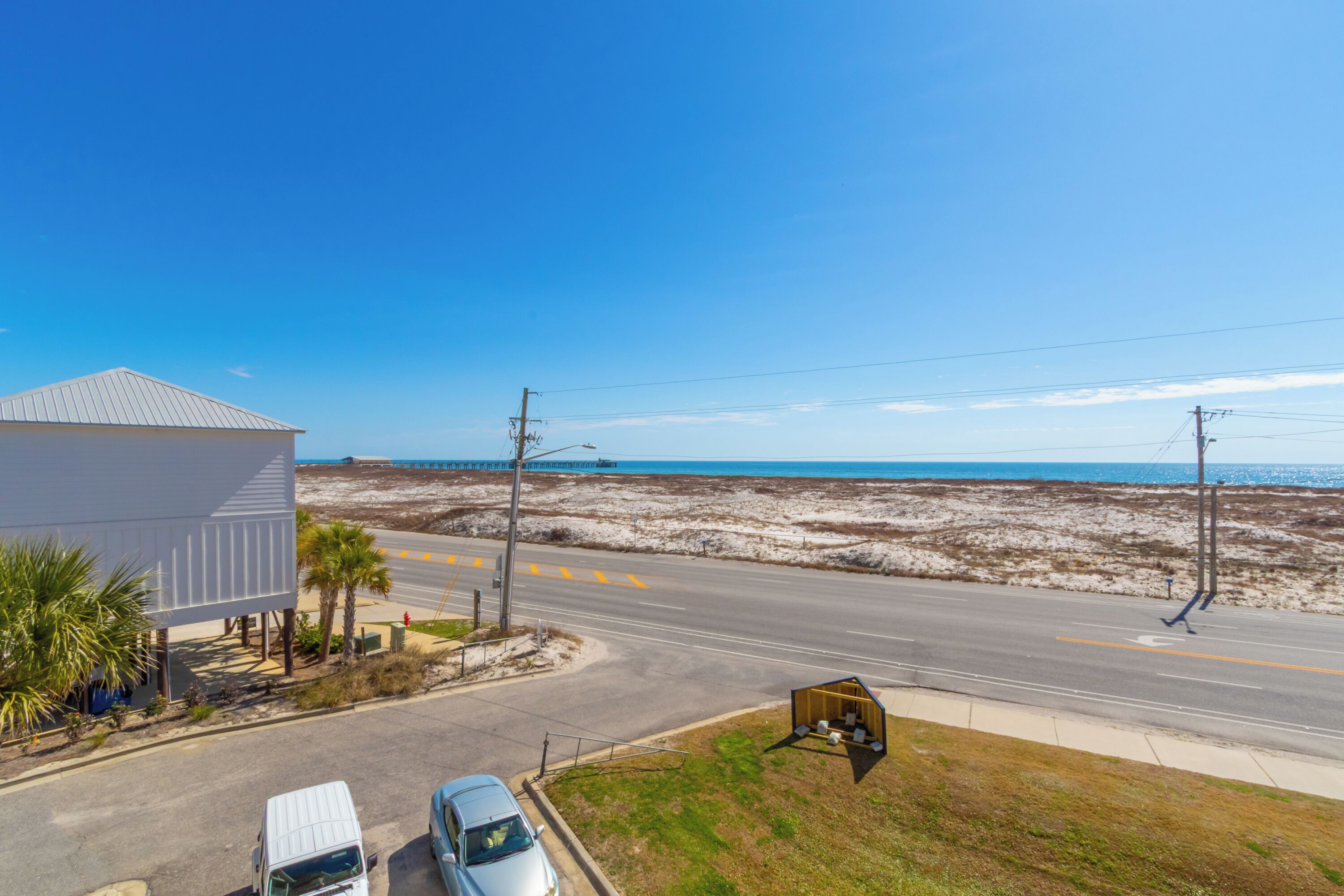A coastal road with a white building, a parked van, and a small shed.