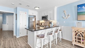 Een moderne keuken met witte kasten, een centraal eiland met barstoelen, en een decoratie aan de muur met een nautisch thema.