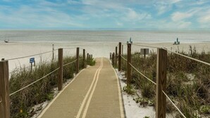 Een zandpad langs het strand dat naar de oceaan leidt, met houten palen en een blauw bord.