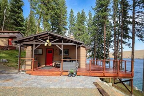 A cabin with a red door, a covered porch, and a deck overlooking a lake. - Prop House | Wallowa lakefront home w/dock (Joseph)