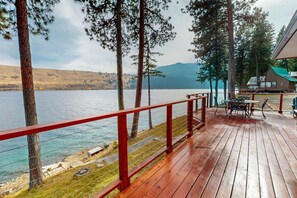 A wooden deck with a red railing overlooking a lake, surrounded by trees and a distant mountain.