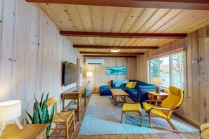 A wooden interior with a sofa, chairs, a TV, and a painting. - Prop House | Wallowa lakefront home w/dock (Joseph)
