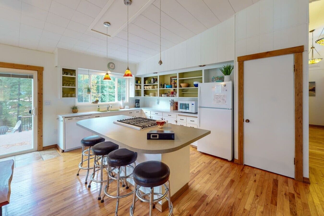 A modern kitchen with a central island, bar stools, and built-in shelves.
