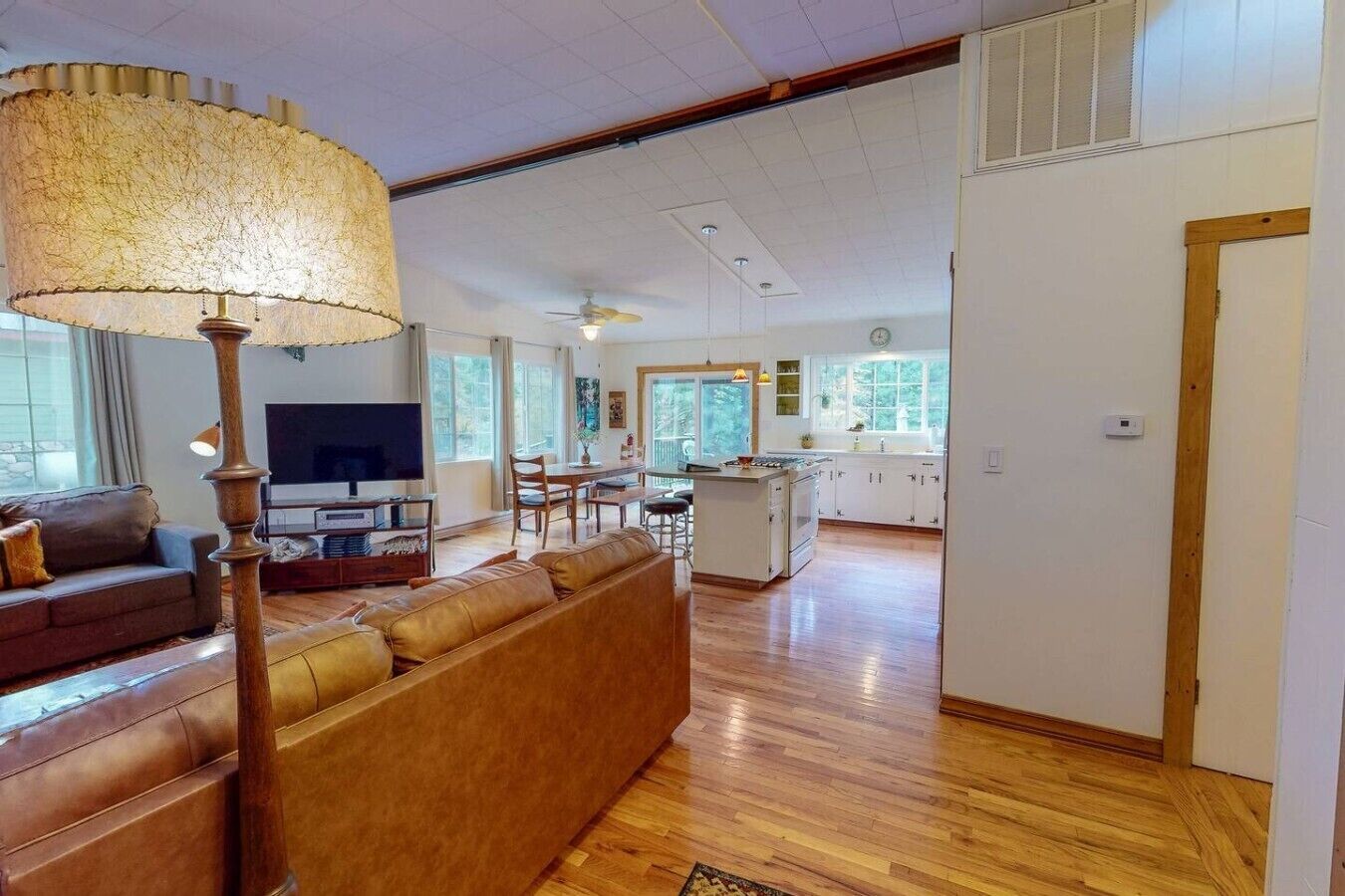 A spacious living room with a sofa, a television, and a dining area with a kitchen in the background.