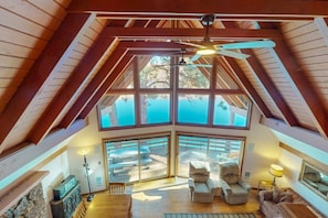 A high-ceilinged room with a large window, a ceiling fan, and a view of the outdoors.