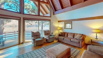 A spacious living area with large windows, a wooden ceiling, and a view of a lake.