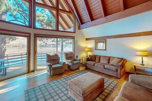A spacious living area with large windows, a wooden ceiling, and a view of a lake.