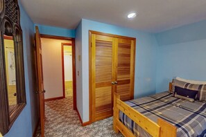 A bedroom with a bed, a wooden wardrobe, a mirror, and a door leading to a bathroom.
