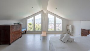 A bedroom with a large window, a wooden dresser, a bed with white linens, and a hanging light fixture. - LA TERRAZZA - Between sky and sea, silence speaks of beauty (Rapallo)