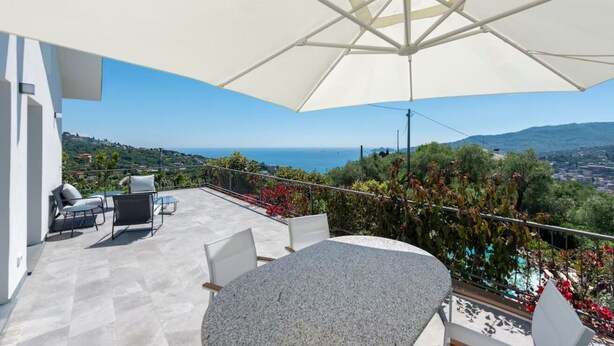 A terrace with a table and chairs, a white umbrella, and a view of the sea and hills. - LA TERRAZZA - Between sky and sea, silence speaks of beauty (Rapallo)
