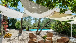 An outdoor seating area with wicker chairs and a table, a pool in the background, and a shaded area with a white canopy. - LA TERRAZZA - Between sky and sea, silence speaks of beauty (Rapallo)