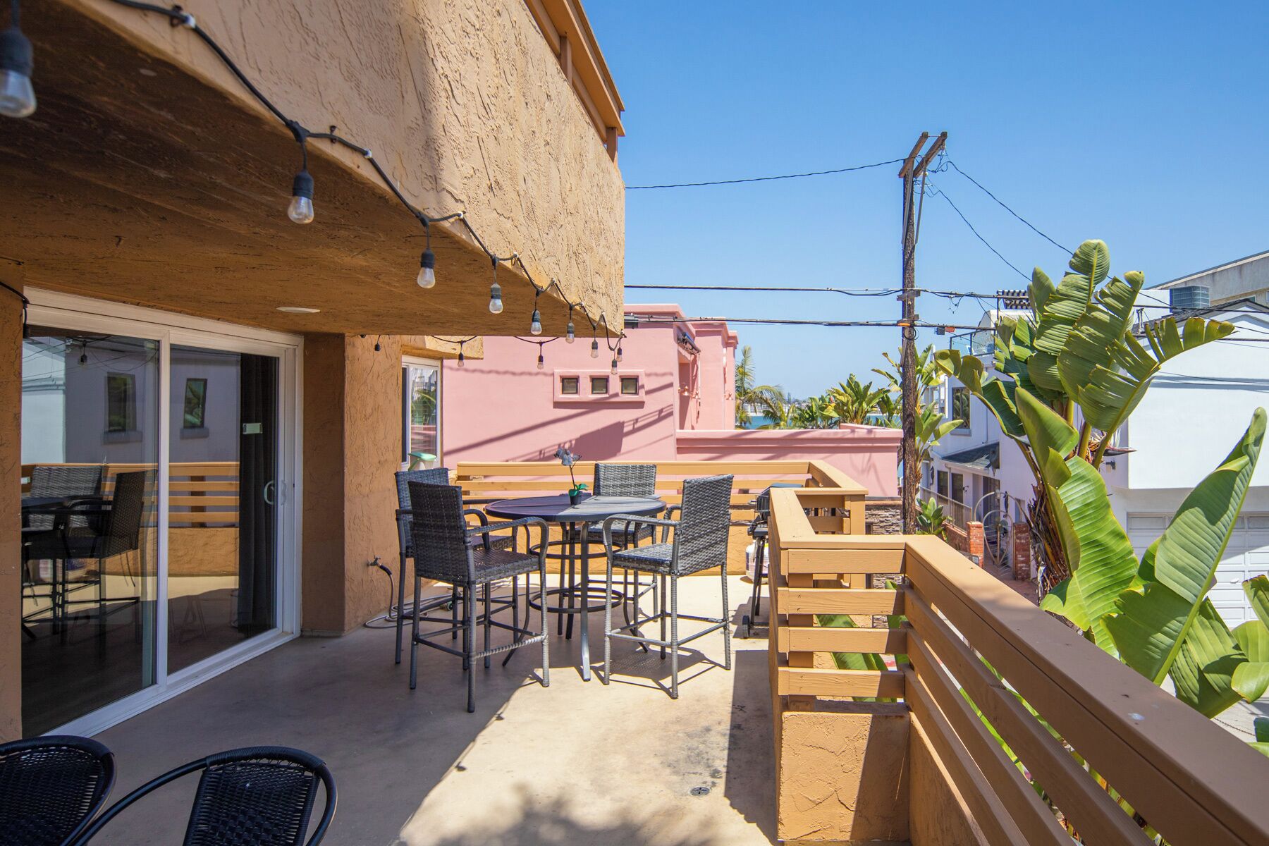 Un espace extérieur aménagé en terrasse, avec des chaises et une table en osier, une clôture en bois et une vue sur les bâtiments voisins.