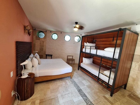 A bedroom with a single bed, a bunk bed, a wooden headboard, a small table, and a wall-mounted heater. - Hotel Kupuri Sayulita (Sayulita)