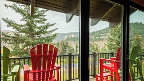 Eine Terrasse mit roten Adirondack-Stühlen, einer Glastür und Blick auf eine bewaldete Landschaft.