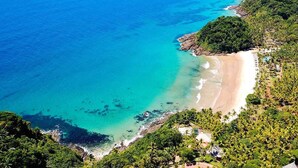 A coastal area with a beach, clear turquoise waters, and dense greenery.