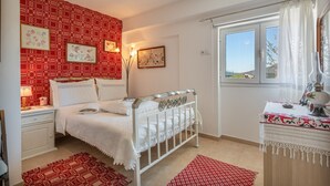 A bedroom with a bed, bedside tables, a window with curtains, and patterned wall and floor rugs.