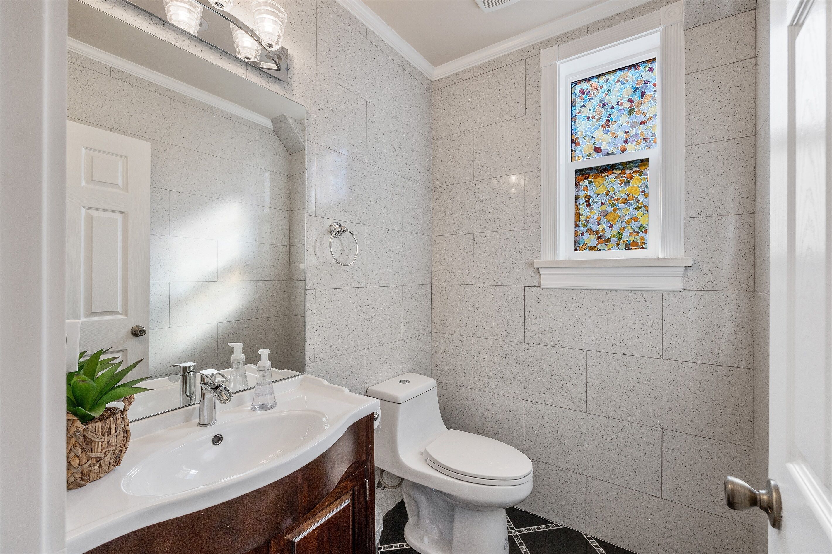 A bathroom with a white sink, a toilet, and a window with a stained glass design.