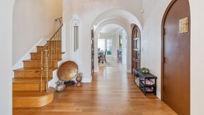 A wooden staircase with a chandelier, a hallway with a shoe rack, and an arched doorway. - Mediterranean Charm Nr Beach/Shopping/EZ Parking (San Francisco)