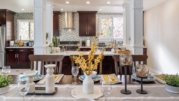 A modern kitchen with dark wood cabinets, a central island, and a dining area set with white and blue plates, glasses, and a vase with yellow flowers. - Mediterranean Charm Nr Beach/Shopping/EZ Parking (San Francisco)