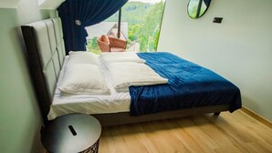 Ein Schlafzimmer mit einem Bett, einem Sessel, einem runden Tisch und Blick auf Grünfläche.