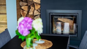 Un intérieur moderne avec une cheminée, une table à manger agrémentée d’un vase de fleurs et une pile de bois de chauffage.