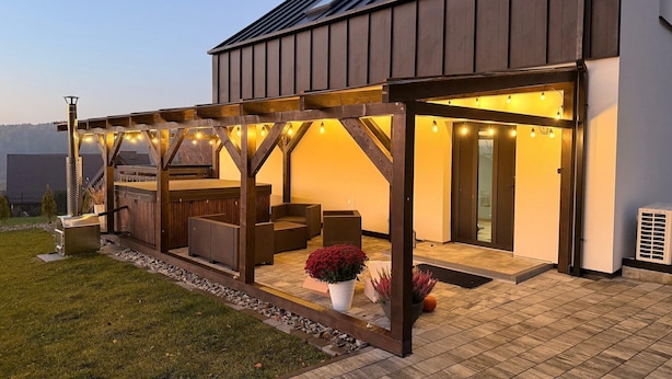 Un espace extérieur aménagé, abrité et doté de mobilier en bois et de guirlandes lumineuses.