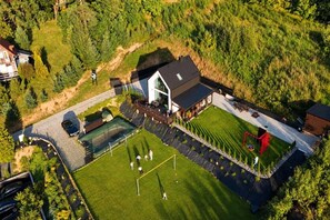 Vista aerea di una proprietà residenziale con un ampio prato, un campo da tennis e una casa con tetto spiovente.