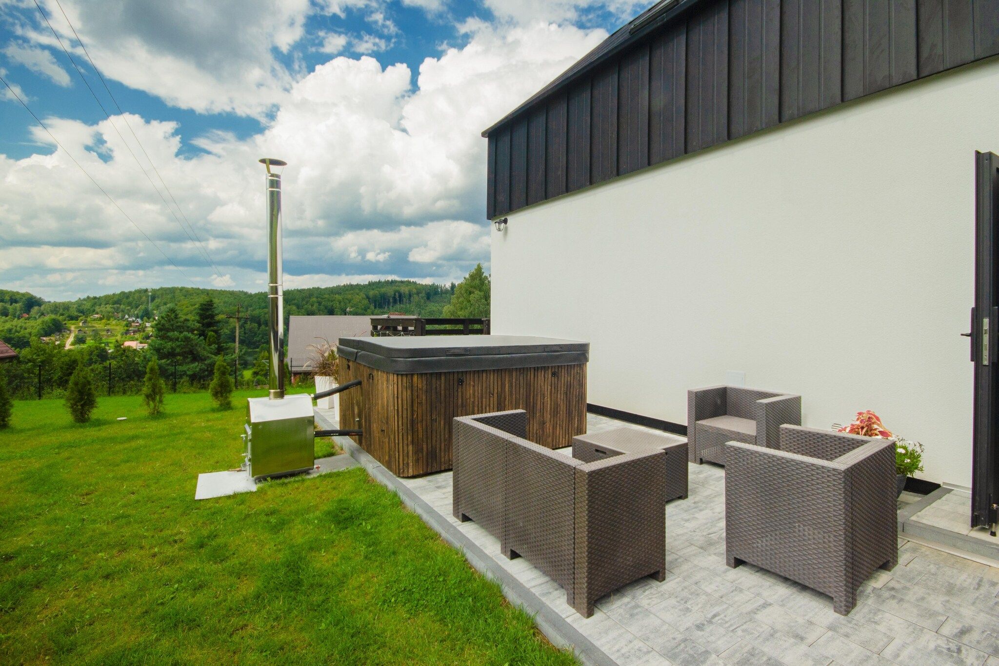 An outdoor patio with wicker furniture, a hot tub, and a view of a green landscape.