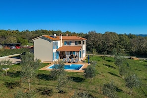 Une maison à deux étages avec une piscine, entourée de verdure et d’arbres.