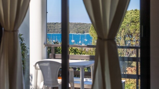 Un balcon avec une table et des chaises, donnant sur une étendue d’eau où naviguent des voiliers.