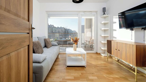 Un salon moderne avec un canapé gris, une table basse blanche, un meuble en bois et un téléviseur fixé au mur.