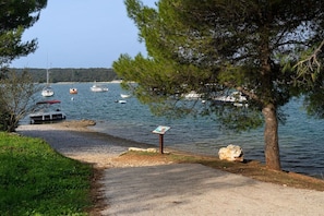 A coastal area with a gravel path leading to the water, boats anchored nearby, and a signpost by the shore. - Apartments Erla (16014-A2) - Banjole (Banjole)