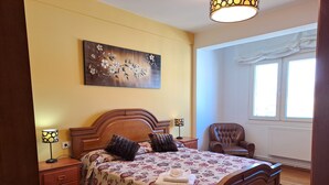 A bedroom with a wooden bed, a nightstand with a lamp, a chair, and a painting on the wall. - Torre Plaza 4. A cozy apartment in Boiro, beaches and terraces. (boiro)