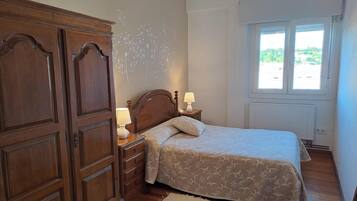 Ein Schlafzimmer mit Holzschrank, einem Bett mit Blumenmuster, Nachttischlampen, einem Fenster mit Aussicht und einer Deckenleuchte.