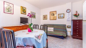 Ein Wohnzimmer mit Esstisch, Sofa, Fernseher und Kunstwerken an den Wänden.
