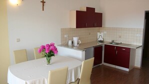 Cocina compacta con comedor, que incluye una mesa blanca, sillas, un jarrón con flores y una cruz en la pared.