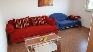 Un salón con un sofá rojo, un sofá azul y una mesa de centro de vidrio con un frutero.